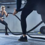 Athletic woman doing battlerope exercise with personal trainer at gym